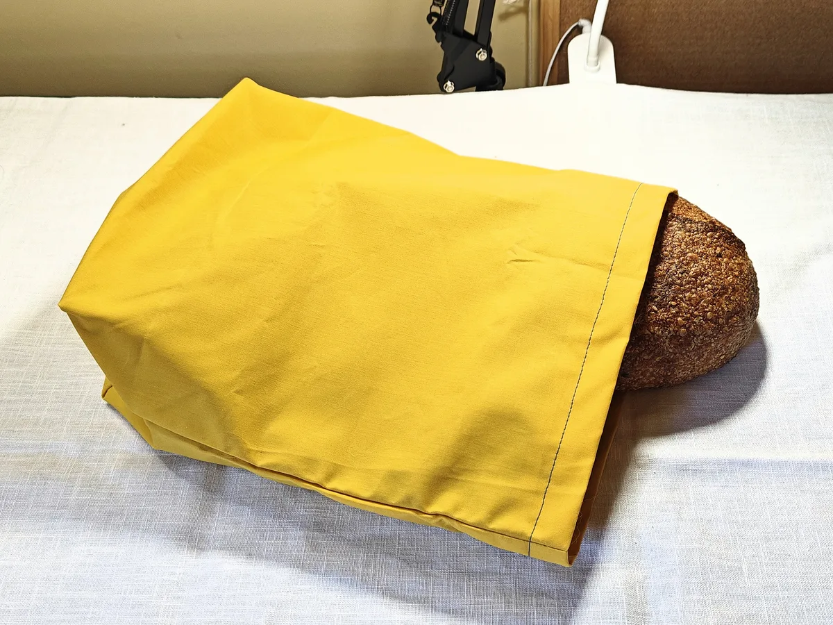 Yellow waxed cotton bread bag with a loaf tucked inside, resting on a light cloth